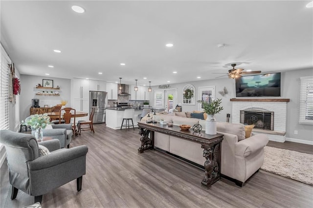 living room featuring a brick fireplace, recessed lighting, a ceiling fan, baseboards, and wood finished floors