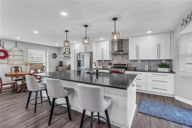 kitchen with dark countertops, appliances with stainless steel finishes, a sink, wall chimney exhaust hood, and tasteful backsplash