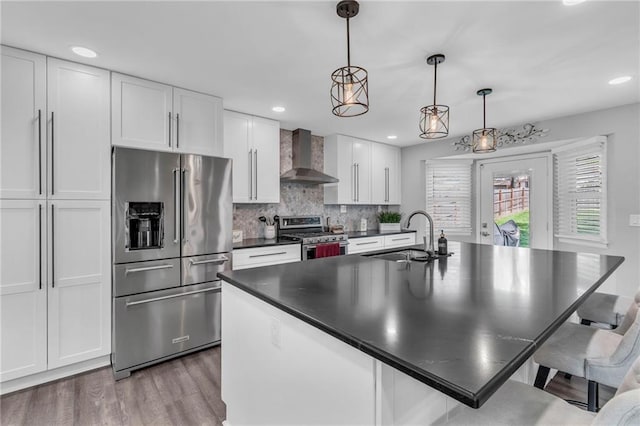 kitchen with wood finished floors, wall chimney range hood, white cabinets, a sink, and stainless steel appliances