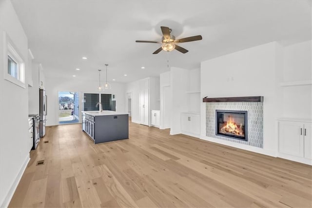 8137 N Farley Ave, Kansas City, MO 64158 - unfurnished living room with a sink, a glass covered fireplace, light wood-style floors, and ceiling fan