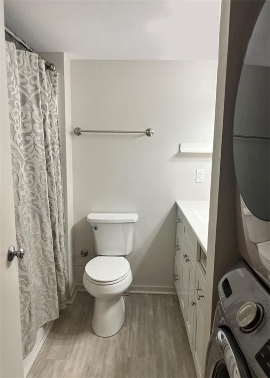 full bathroom with baseboards, toilet, stacked washing maching and dryer, vanity, and wood finished floors