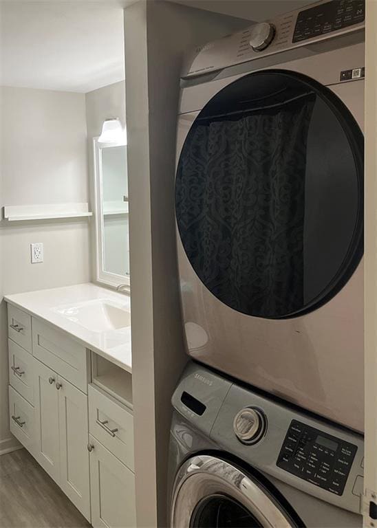 washroom with a sink, light wood-style flooring, stacked washer / drying machine, and laundry area