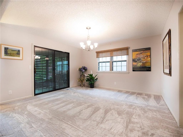 carpeted empty room with baseboards, a textured ceiling, and a notable chandelier