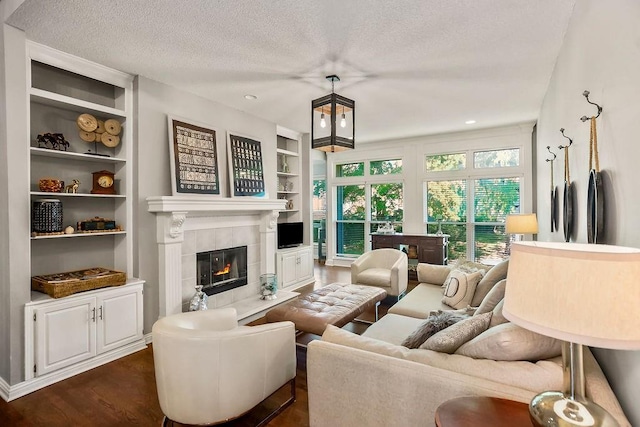 living room featuring dark wood-type flooring, a fireplace, a textured ceiling, and built in shelves