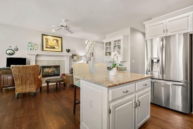 kitchen with stainless steel refrigerator with ice dispenser, white cabinetry, dark wood-type flooring, and a kitchen island