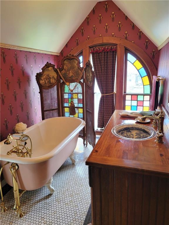 full bath featuring a freestanding tub, vanity, wallpapered walls, and vaulted ceiling