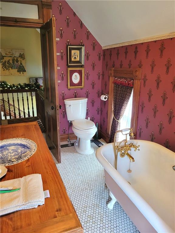 full bath featuring a soaking tub, wallpapered walls, toilet, and lofted ceiling