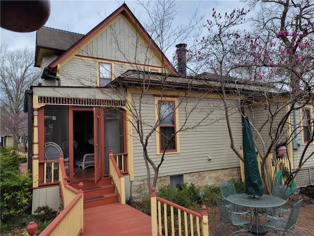 back of property with a chimney, outdoor dining space, and a sunroom