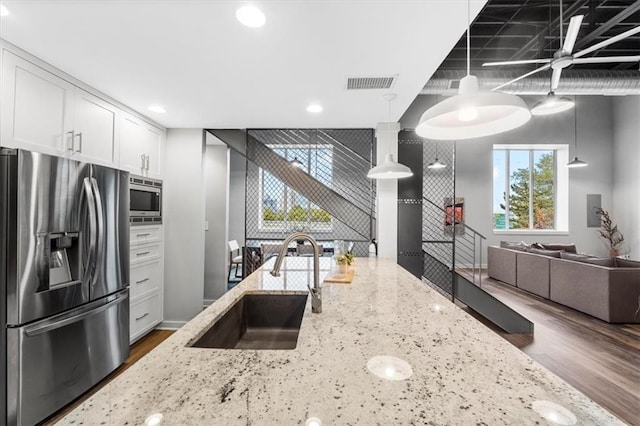 kitchen featuring appliances with stainless steel finishes, a sink, light stone counters, white cabinetry, and dark wood-type flooring