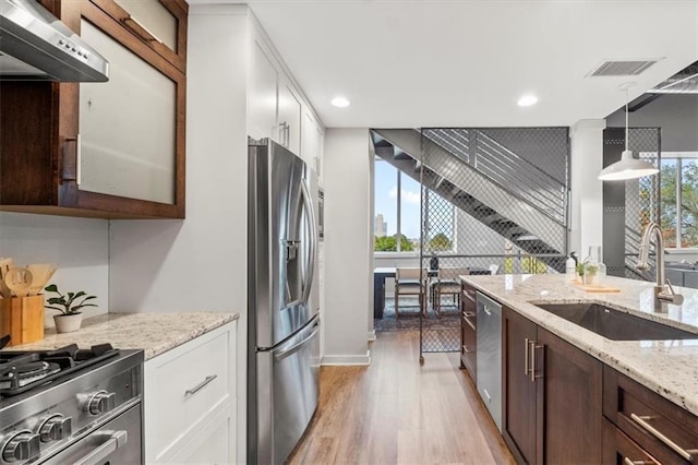 kitchen featuring ventilation hood, a sink, stainless steel appliances, white cabinetry, and light wood-type flooring