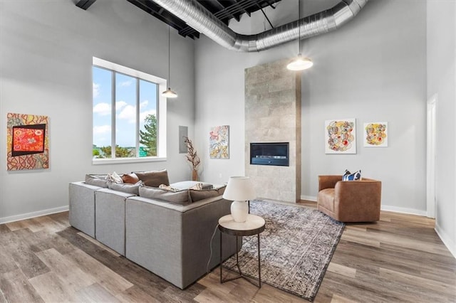 living area with a fireplace, baseboards, wood finished floors, and a towering ceiling