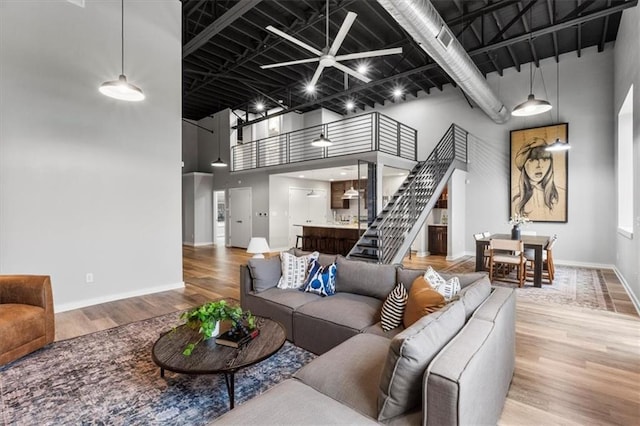 living room with a towering ceiling, wood finished floors, baseboards, ceiling fan, and stairway