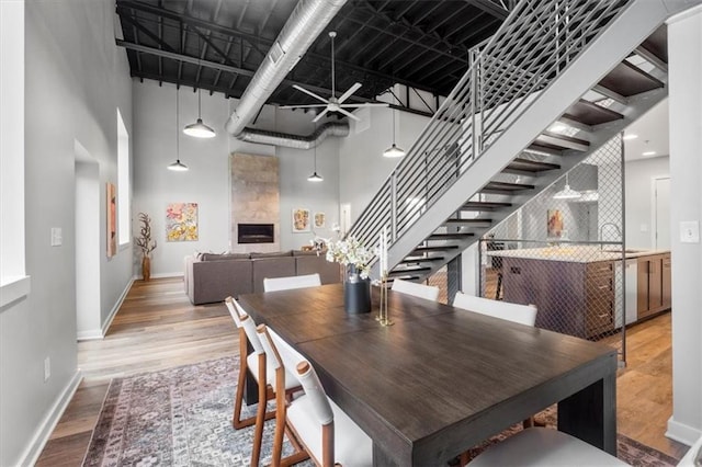 dining room featuring a ceiling fan, a towering ceiling, wood finished floors, baseboards, and stairs