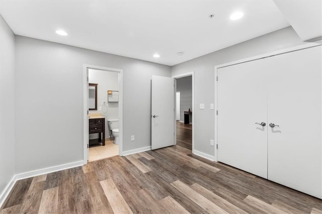 unfurnished bedroom with a closet, wood finished floors, baseboards, recessed lighting, and ensuite bath