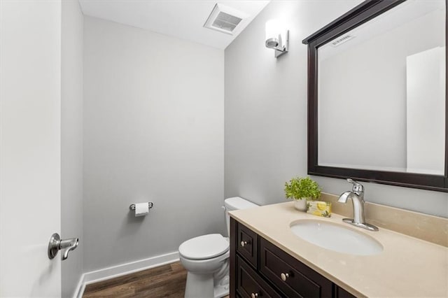 half bath featuring visible vents, wood finished floors, baseboards, vanity, and toilet