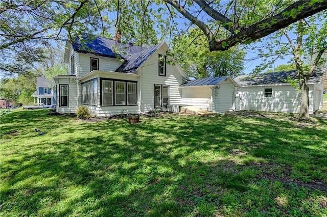 back of house with metal roof, a sunroom, a standing seam roof, an outbuilding, and a yard