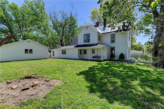 rear view of property featuring a chimney, fence, metal roof, and a yard