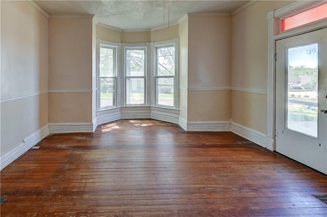 empty room with hardwood / wood-style floors, crown molding, and baseboards