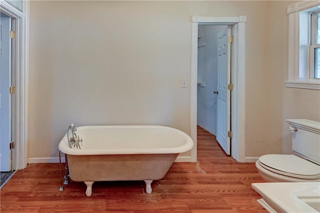 full bath with a freestanding tub, toilet, wood finished floors, and baseboards