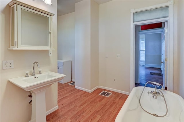 bathroom featuring a tub, baseboards, visible vents, and wood finished floors