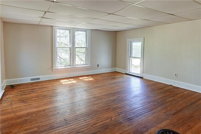 spare room featuring a healthy amount of sunlight, visible vents, a drop ceiling, and wood finished floors