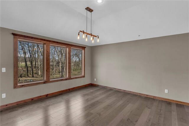 unfurnished room featuring baseboards, wood finished floors, a chandelier, and vaulted ceiling