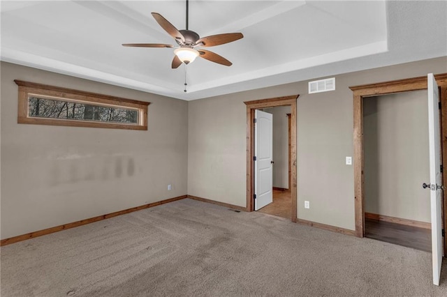 unfurnished bedroom with carpet, visible vents, a tray ceiling, and baseboards