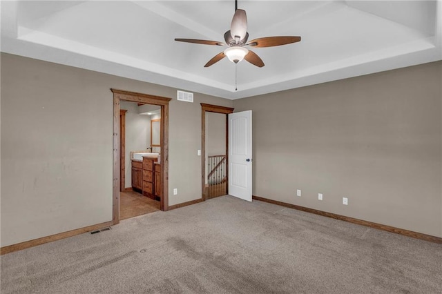 unfurnished bedroom featuring carpet, visible vents, a tray ceiling, and baseboards