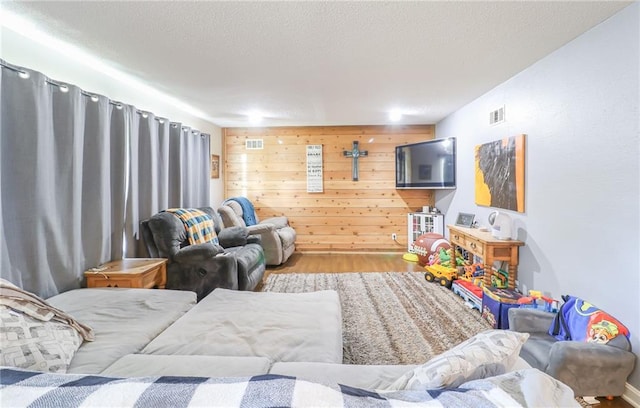 living area featuring wooden walls, visible vents, a textured ceiling, and wood finished floors