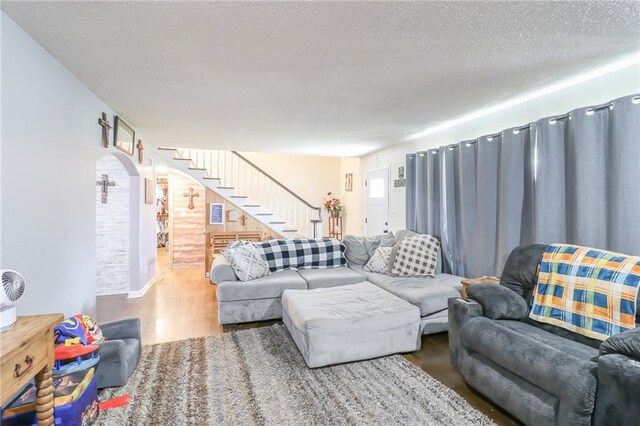 living room with a textured ceiling, arched walkways, wood finished floors, and stairs