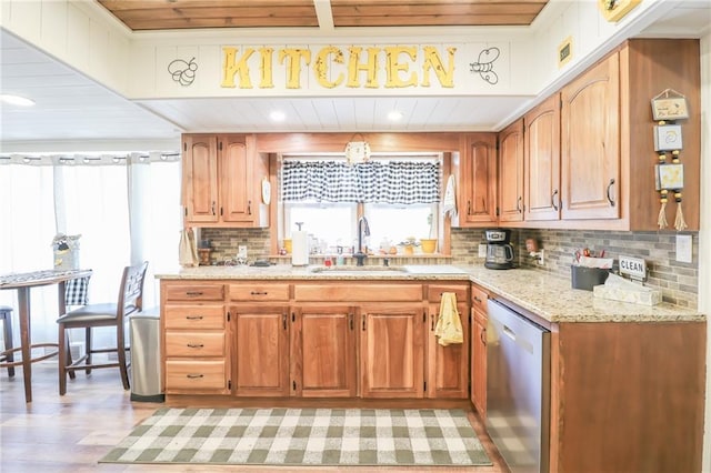 kitchen featuring tasteful backsplash, light stone counters, light wood finished floors, dishwasher, and a sink