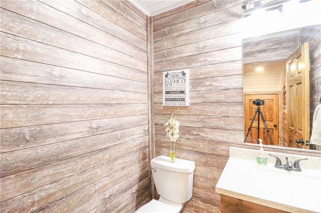 bathroom with wooden walls, vanity, and toilet