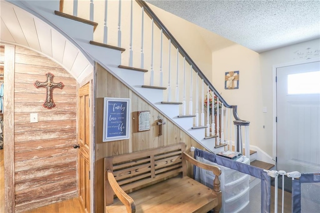 stairway featuring a textured ceiling, wood finished floors, and wooden walls
