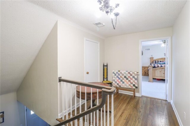 hallway with an upstairs landing, visible vents, a textured ceiling, and wood finished floors