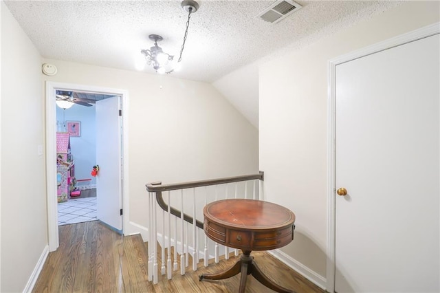 hallway with baseboards, an upstairs landing, a textured ceiling, visible vents, and wood finished floors