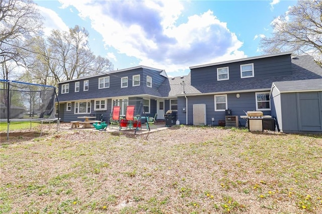 rear view of house featuring a patio area, a yard, a trampoline, an outdoor structure, and a storage unit