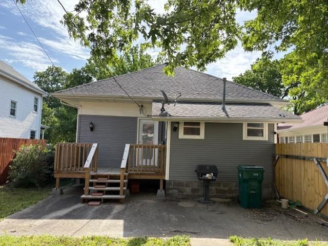 rear view of house with fence, a wooden deck, and a shingled roof
