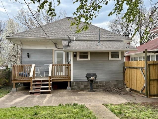 back of property featuring a shingled roof, a wooden deck, fence, and a patio