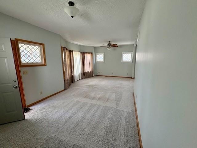 unfurnished living room featuring ceiling fan, light colored carpet, a textured ceiling, and baseboards