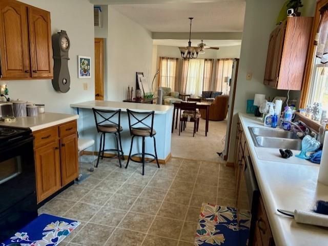 kitchen with black electric range, a sink, brown cabinetry, light countertops, and a peninsula