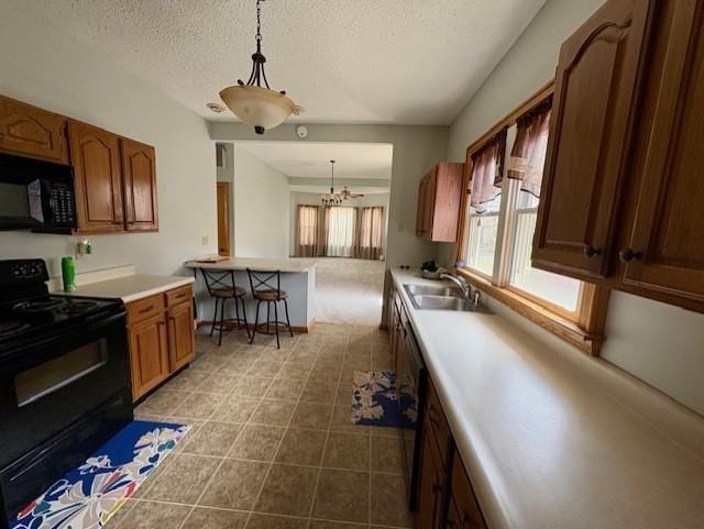 kitchen featuring black appliances, a textured ceiling, a sink, light countertops, and decorative light fixtures
