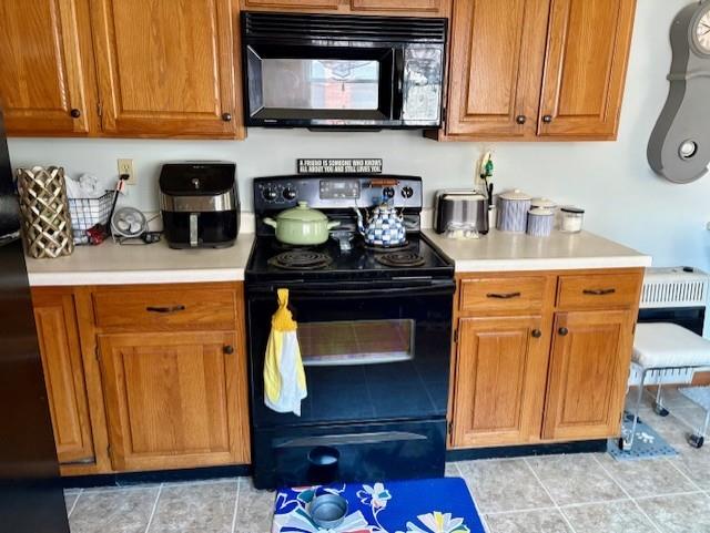 kitchen with black appliances, light countertops, brown cabinets, and light tile patterned floors
