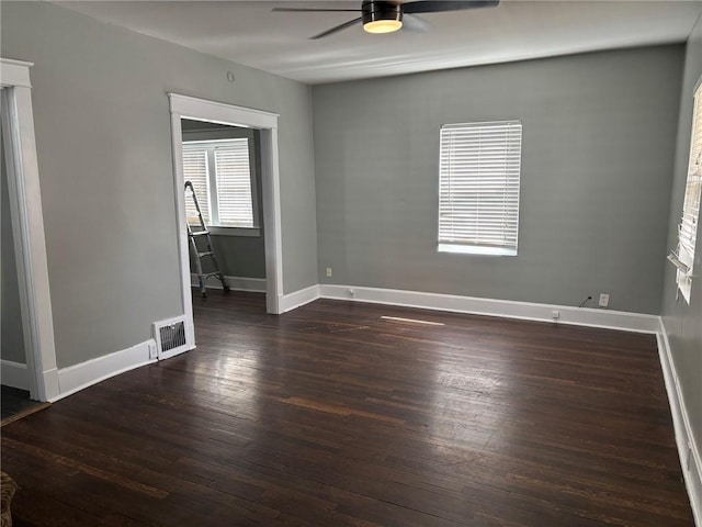 spare room with dark wood-style flooring, baseboards, ceiling fan, and visible vents