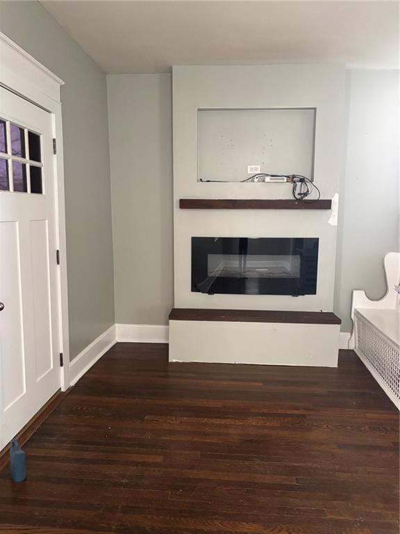 unfurnished living room featuring baseboards, wood finished floors, and a glass covered fireplace