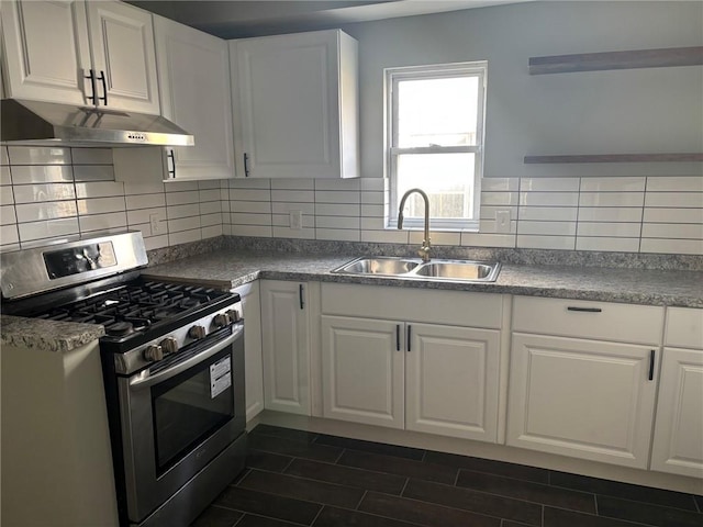 kitchen featuring stainless steel gas stove, a sink, under cabinet range hood, white cabinets, and decorative backsplash