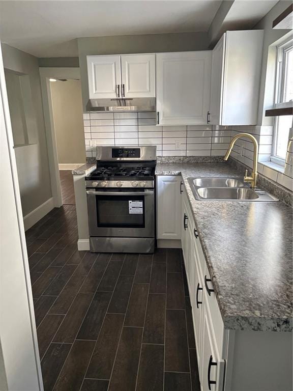 kitchen featuring under cabinet range hood, white cabinetry, stainless steel gas range oven, a sink, and wood tiled floor