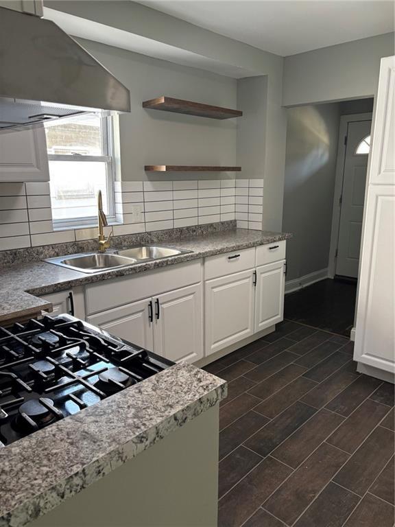 kitchen featuring a sink, open shelves, wall chimney exhaust hood, wood finish floors, and white cabinets