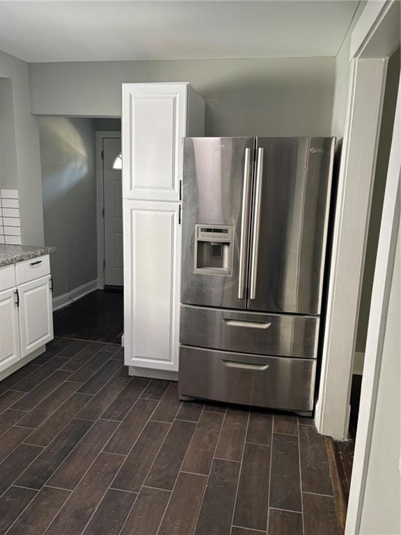 kitchen with light stone countertops, stainless steel fridge, baseboards, wood tiled floor, and white cabinets