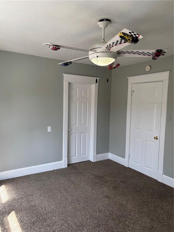 spare room featuring baseboards, a textured ceiling, a ceiling fan, and dark colored carpet