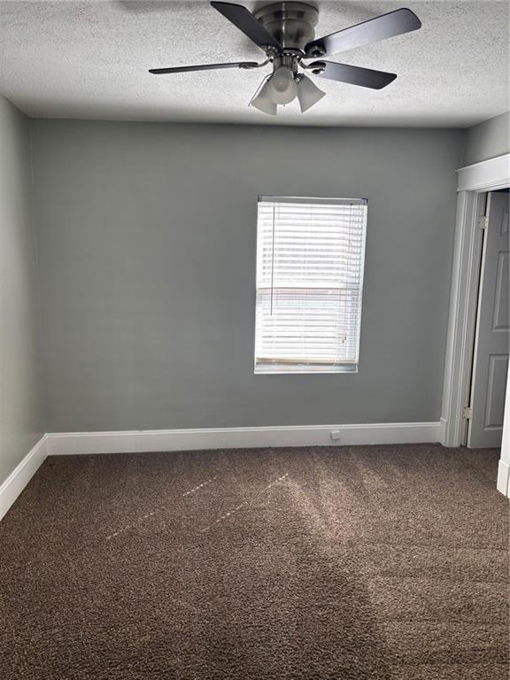 carpeted empty room with a ceiling fan, baseboards, and a textured ceiling